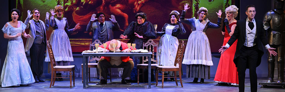 Ensemble of stage actors in period costumes react in shock around a dining table during a theatrical performance.