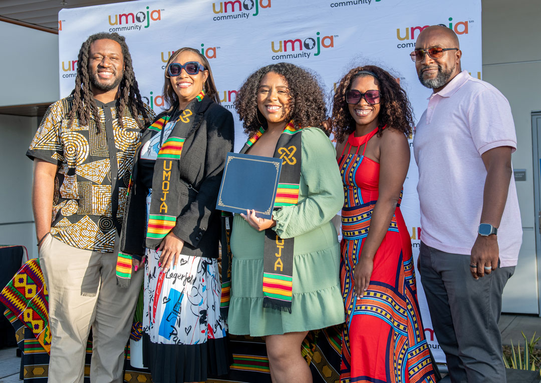 Group of five individuals posing together at an Umoja Community event, wearing colorful stoles and celebrating a special achievement.